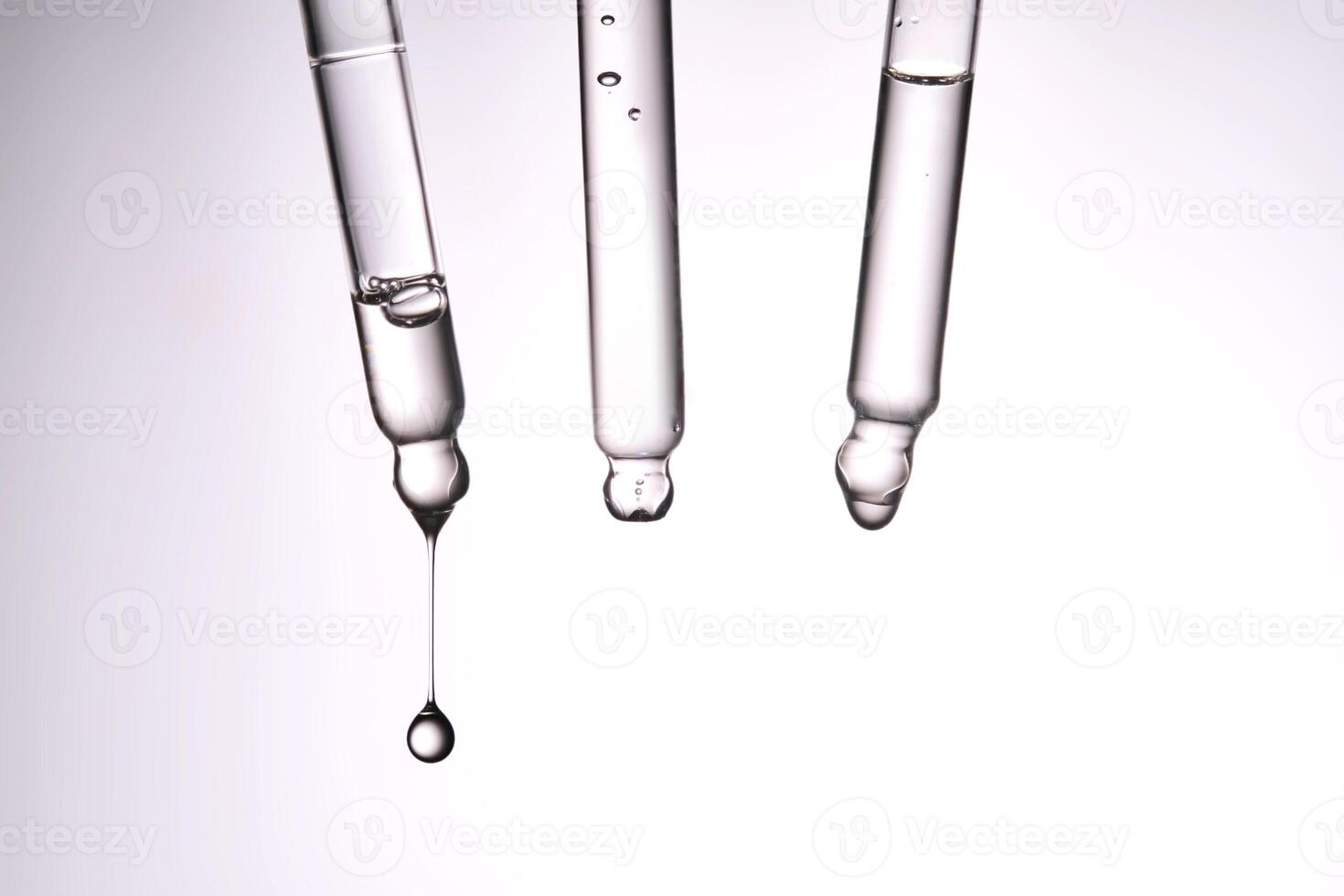 Three pipettes with a cosmetic product. Serum or fluid drips from one of them. photo