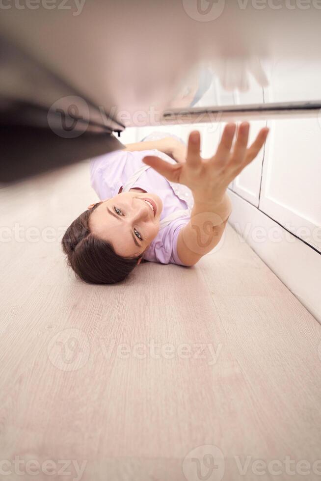 Woman reaching under furniture for lost item in modern home interior, expressing determination and focus. photo