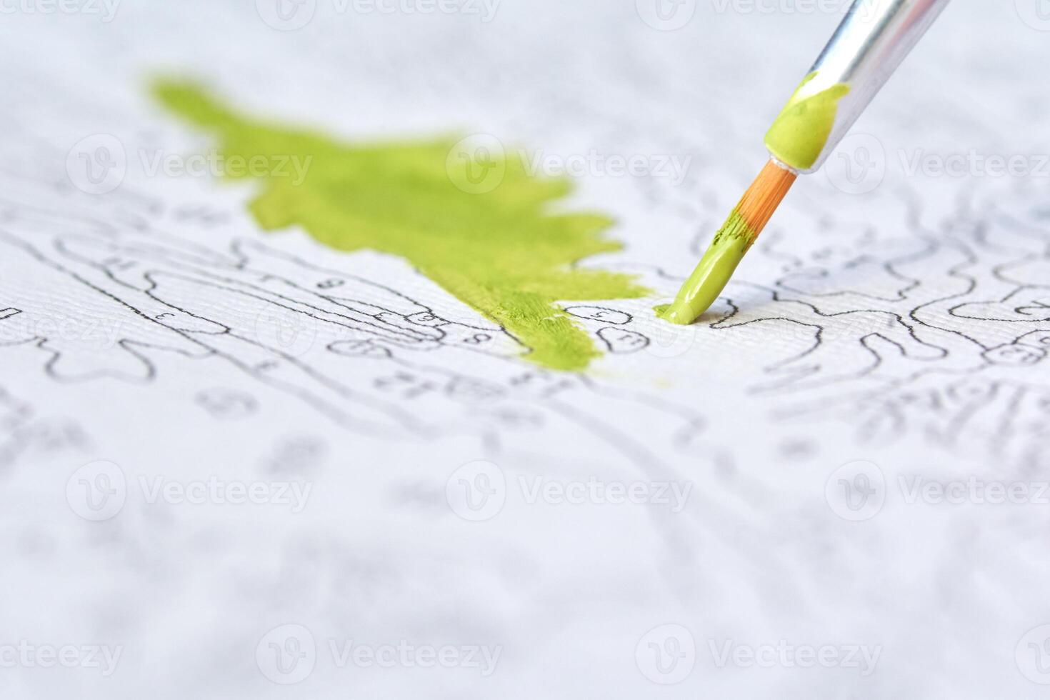Close-up of paintbrush adding vibrant green paint to detailed paint-by-numbers canvas art project. photo