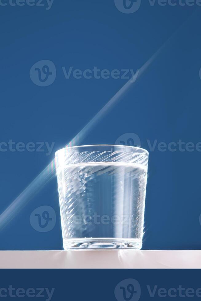 Glass of clean filtered water on blue background with beautiful glare. photo