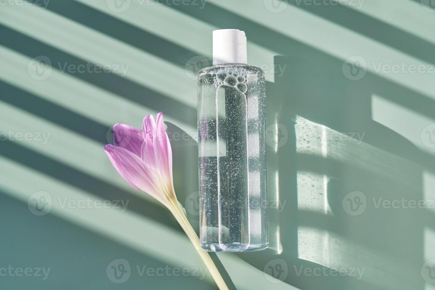 Bottle of facial toner or cleanser on a green background with stripes shadows. photo
