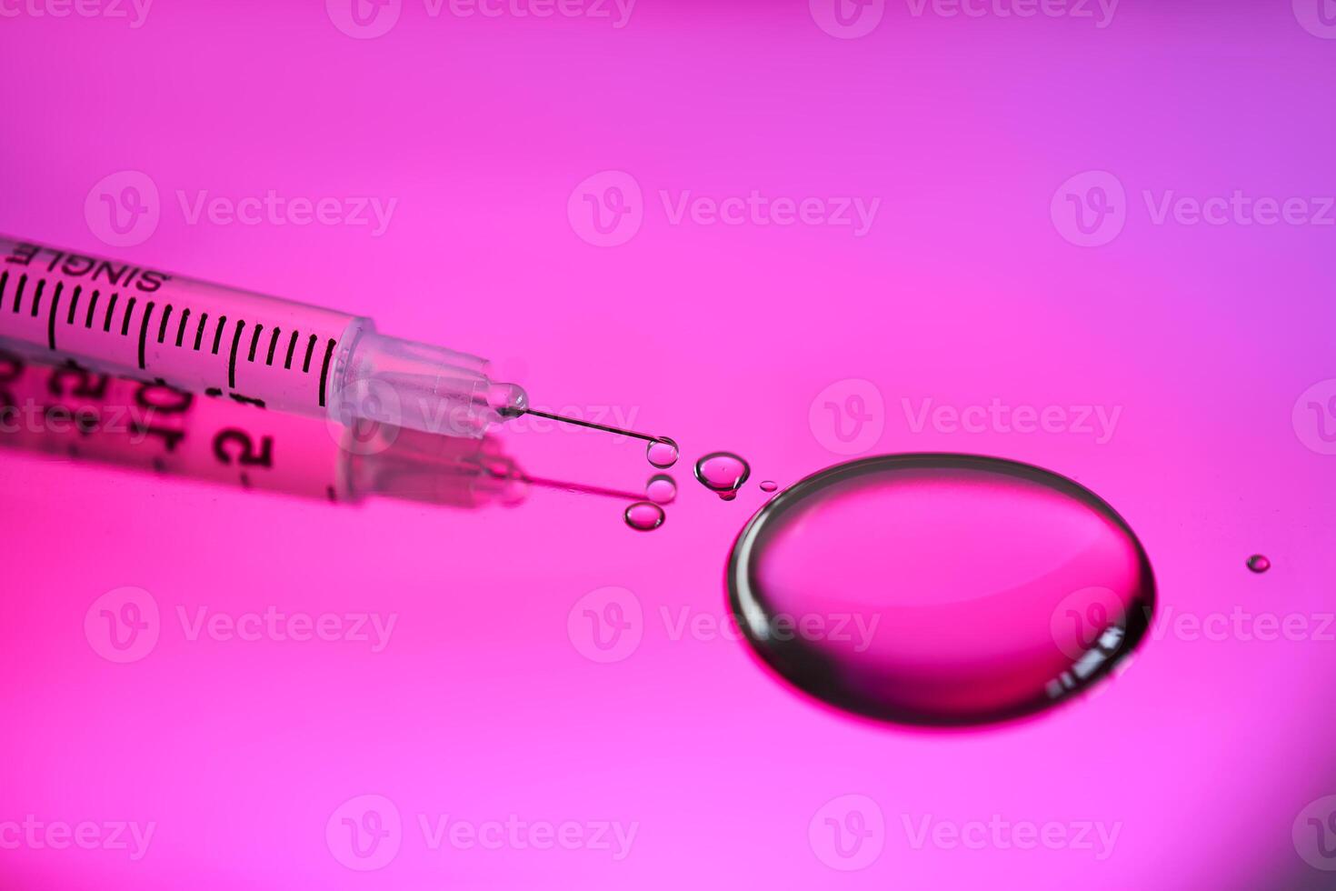 Injection syringe with a drop of drug on a rich pink background. photo