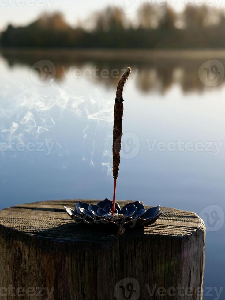 A small incense stick sitting on a wooden post near a lake photo