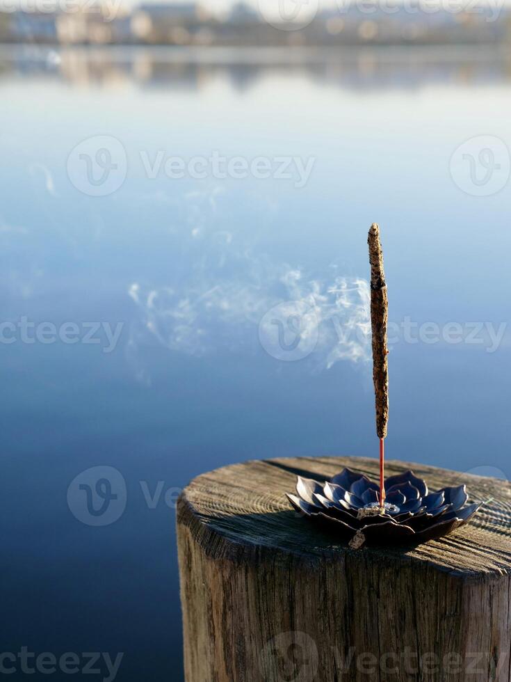 A small incense stick sitting on a wooden post near a lake photo