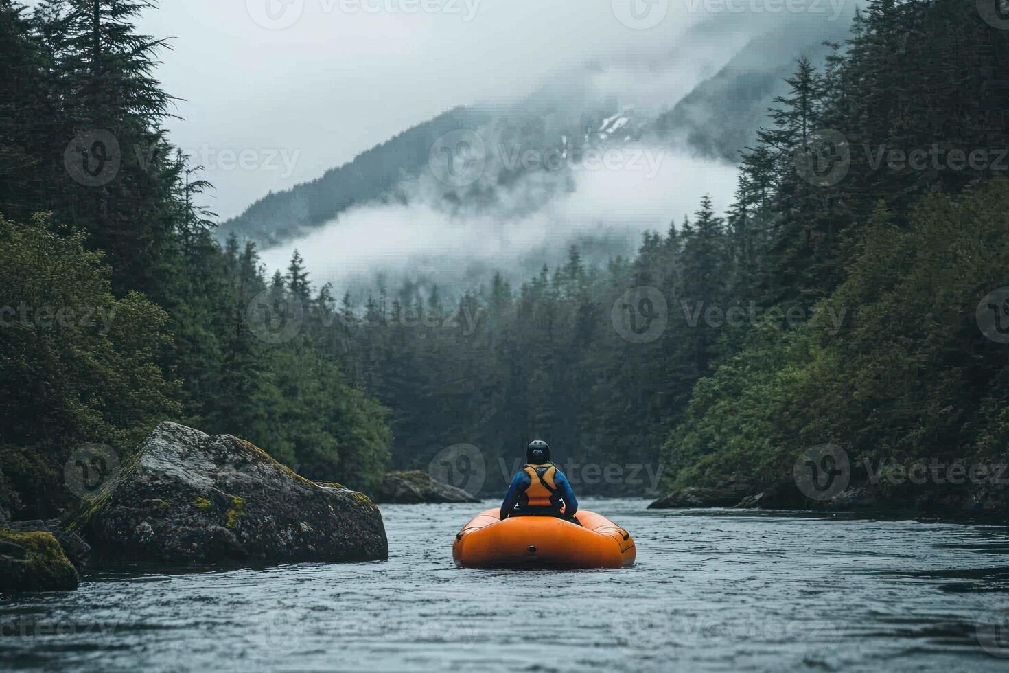 A lone rafter navigates a river surrounded by lush greenery and fog-covered mountains. photo