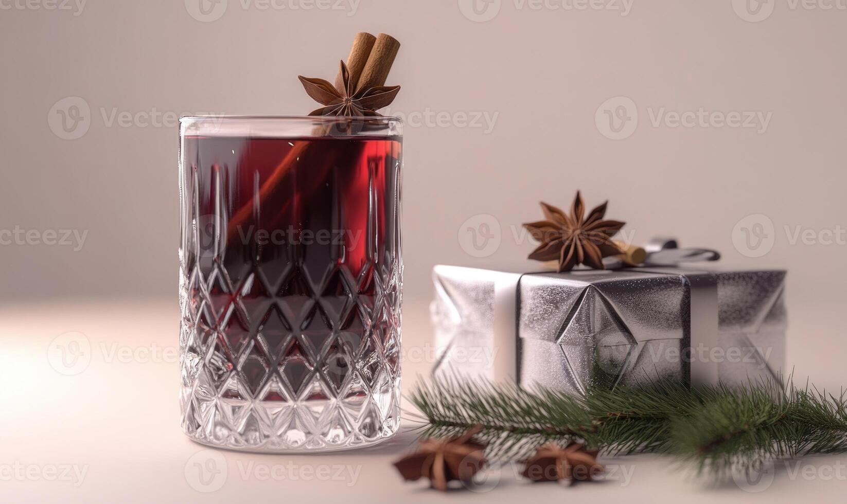 A glass of red wine with cinnamon sticks on top sits next to a silver gift box photo