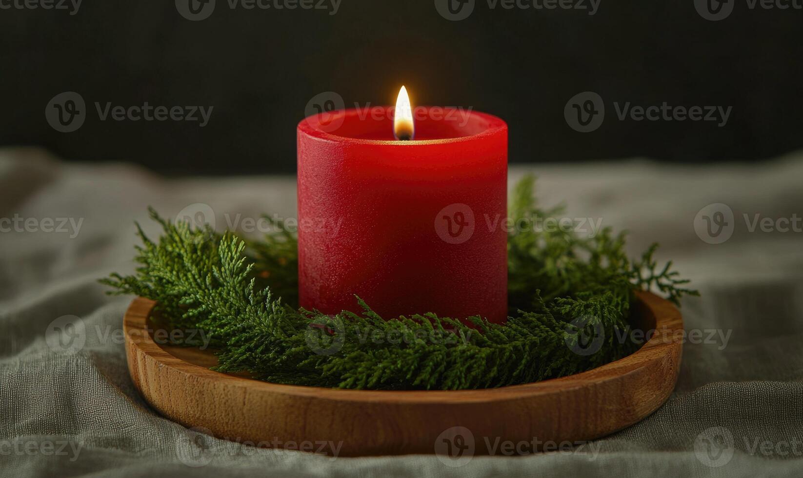 A red candle is lit on a wooden tray with green leaves photo