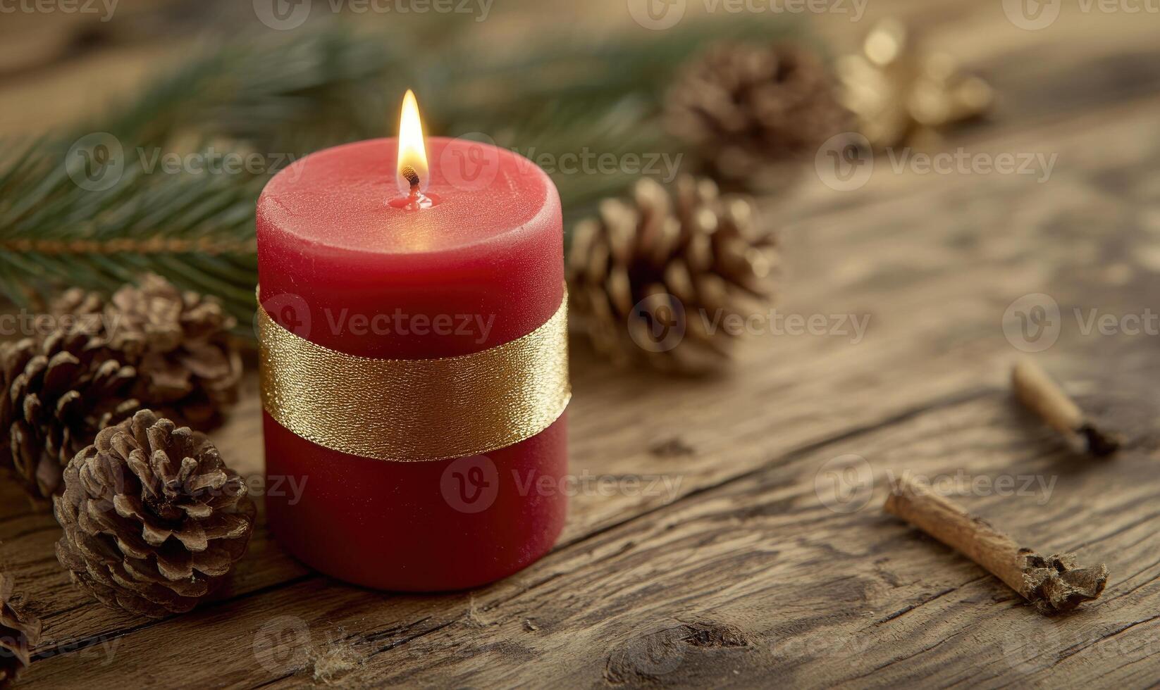 A red candle with gold trim sits on a wooden table next to pine cones photo