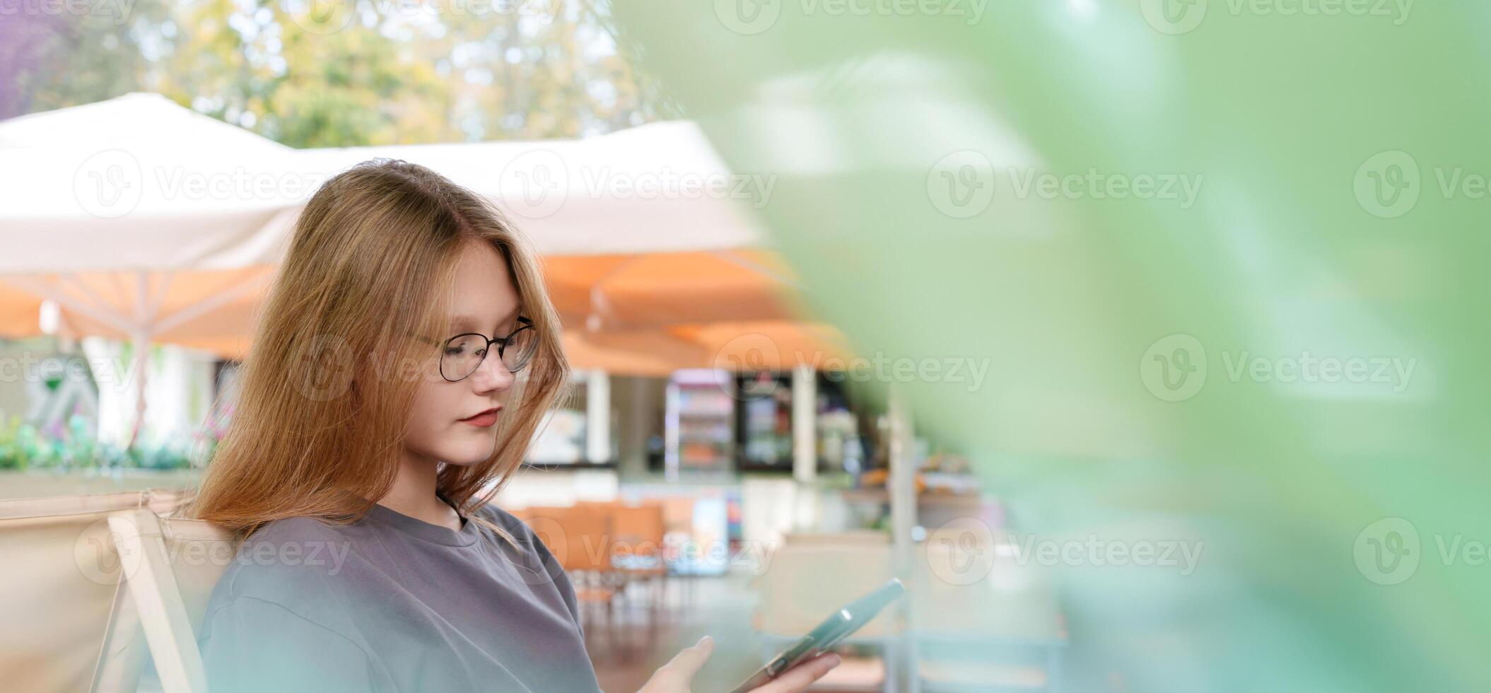 thoughtful teenage girl sits alone at a table in a summer cafe with a cell phone in his hand, her pensive expression hinting at an introspective moment of contemplation photo
