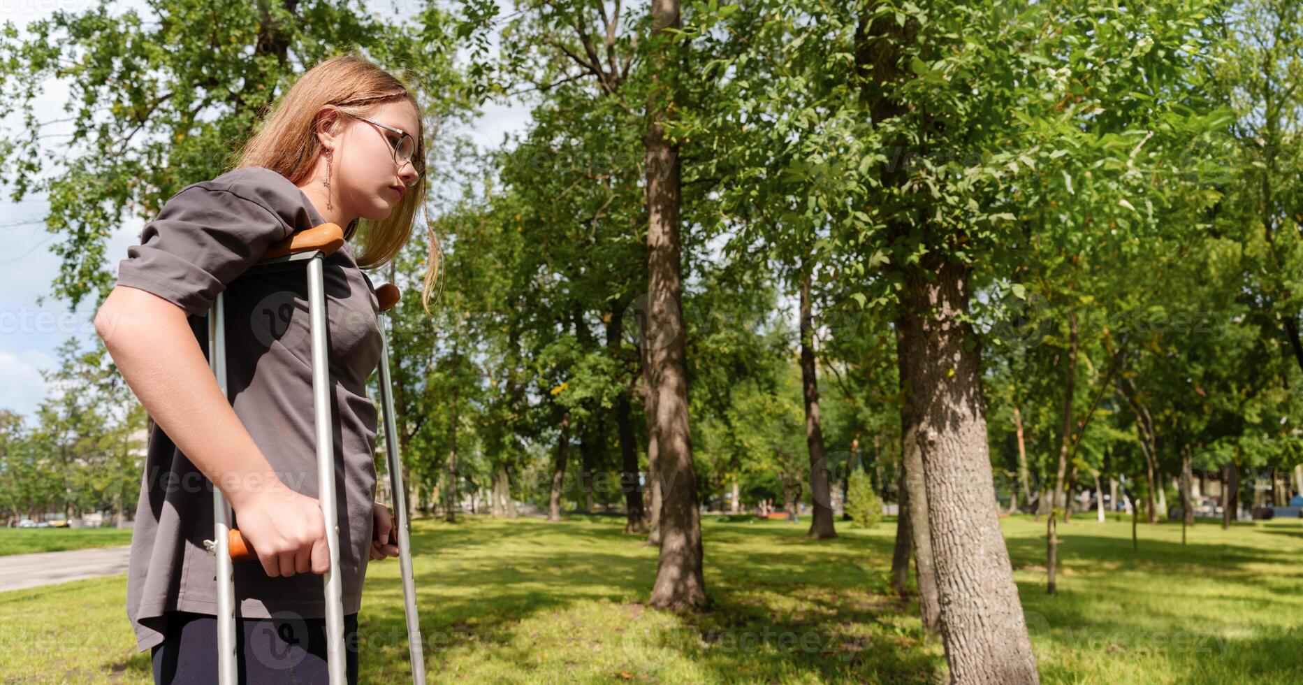 determined girl, navigating the park with her crutches, exudes an air of resilience and empowerment, her gaze fixed forward as she embraces her journey photo