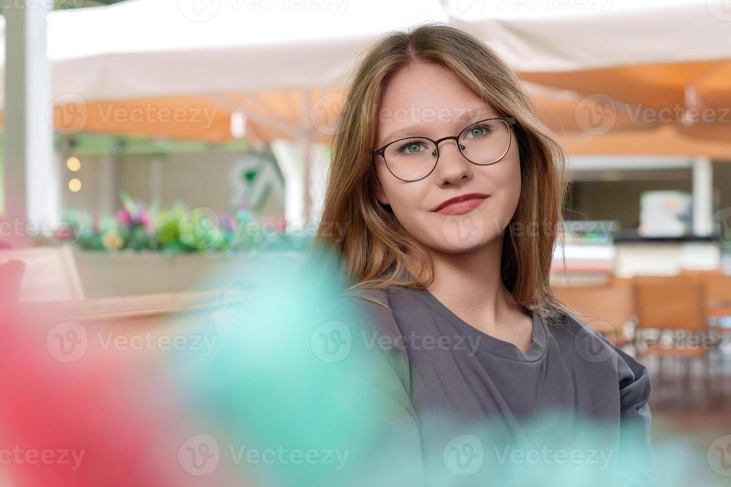 fair-haired teenage girl sits quietly at a table in a summer cafe, her expression thoughtful and her gaze introspective as she loses herself in silent contemplation photo