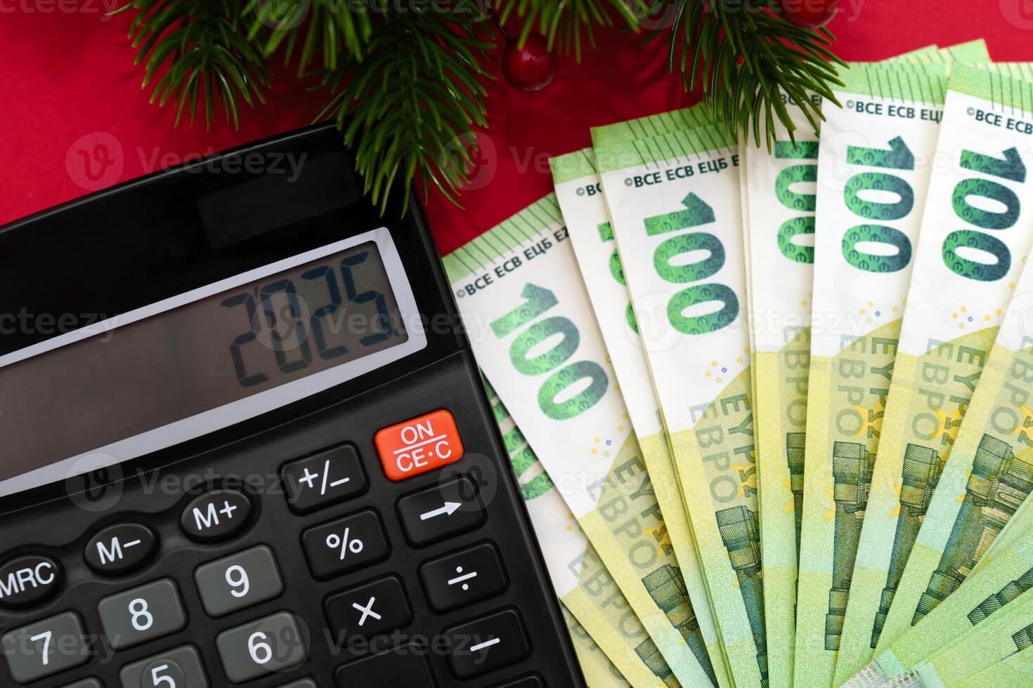 Calculator, 100 euro banknotes and the inscription 2025 new year with spruce branches on a red background, economic crisis, tax time photo