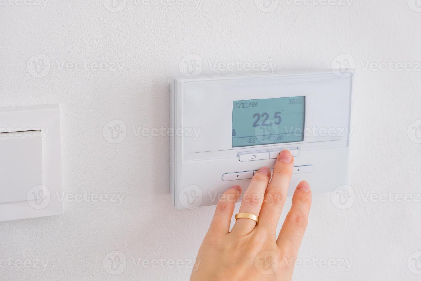 Hand adjusting digital thermostat on wall to control room temperature photo