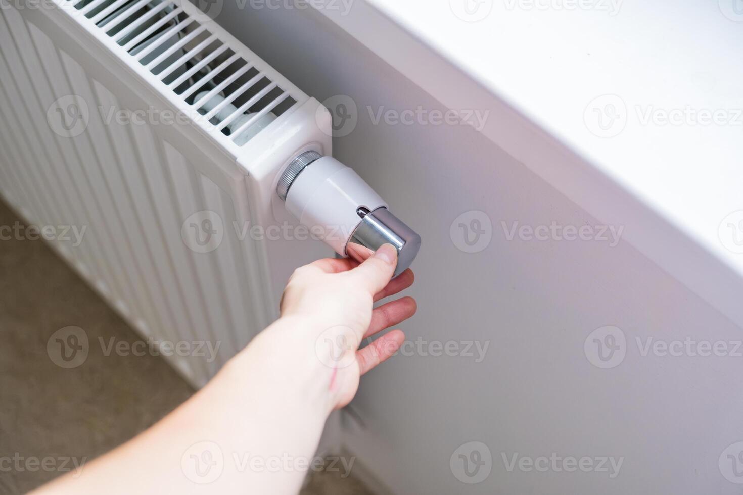 Woman regulates temperature at home with the heating knob on room battery photo