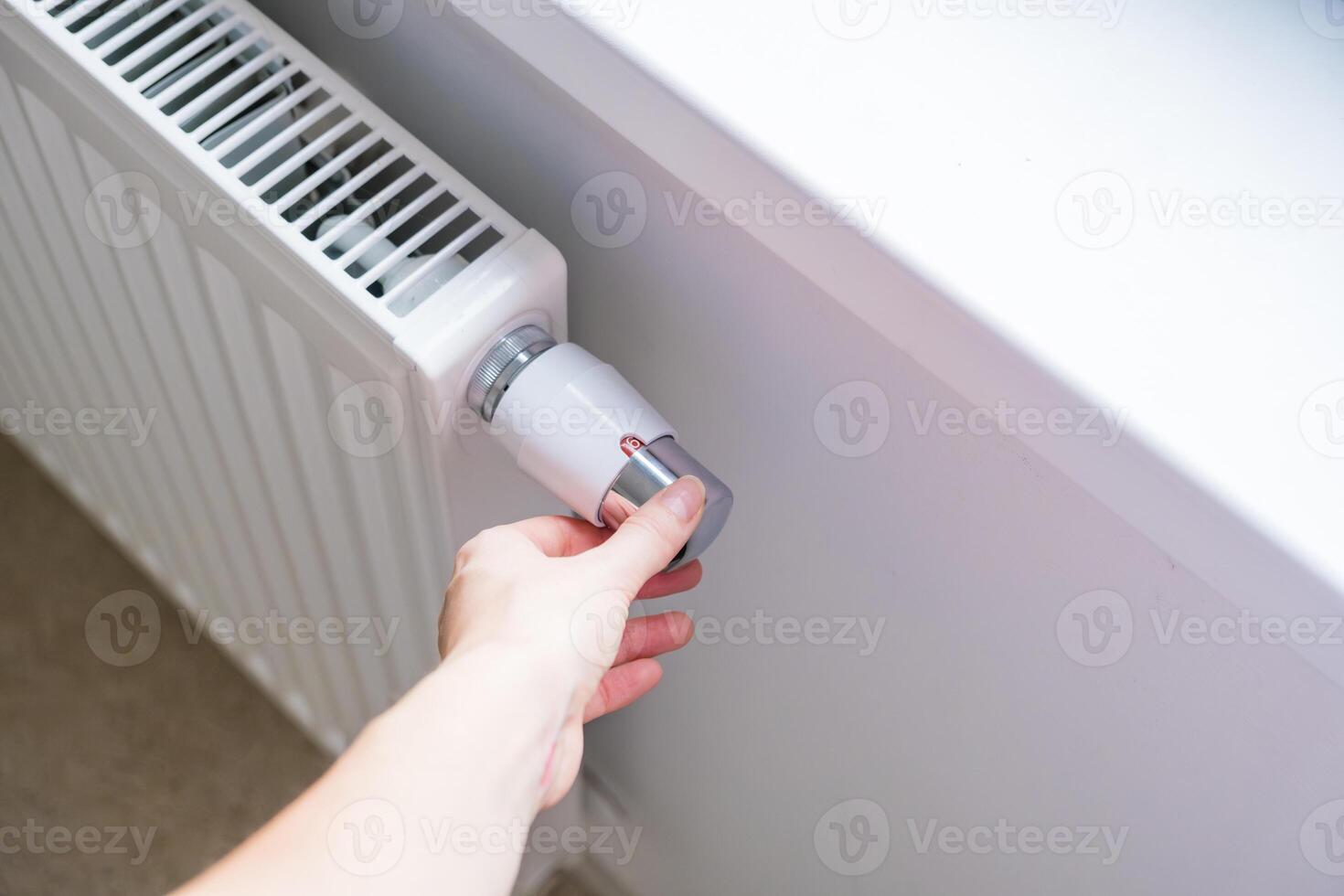 Woman regulates temperature at home with the heating knob on room battery photo
