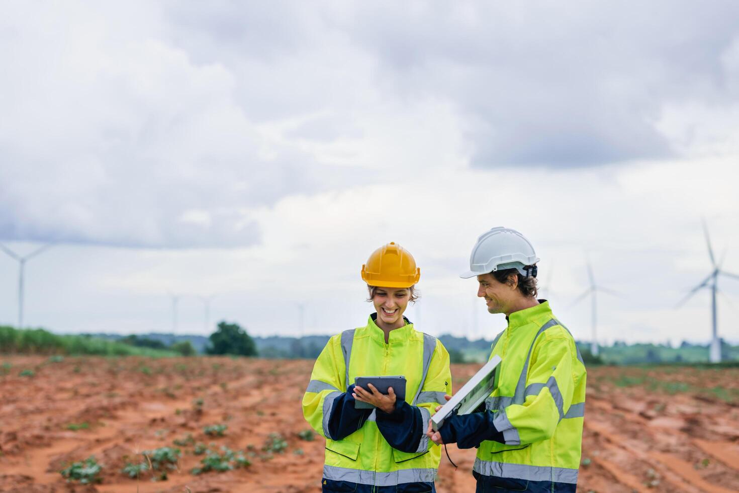 Two people wearing safety gear and holding tablets, looking at something on the screen. Scene is serious and focused photo