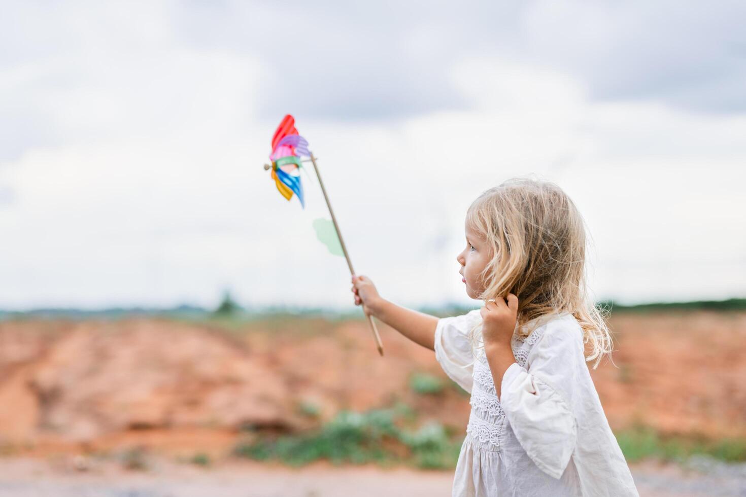 young girl is holding a windmill toy and standing in a field photo