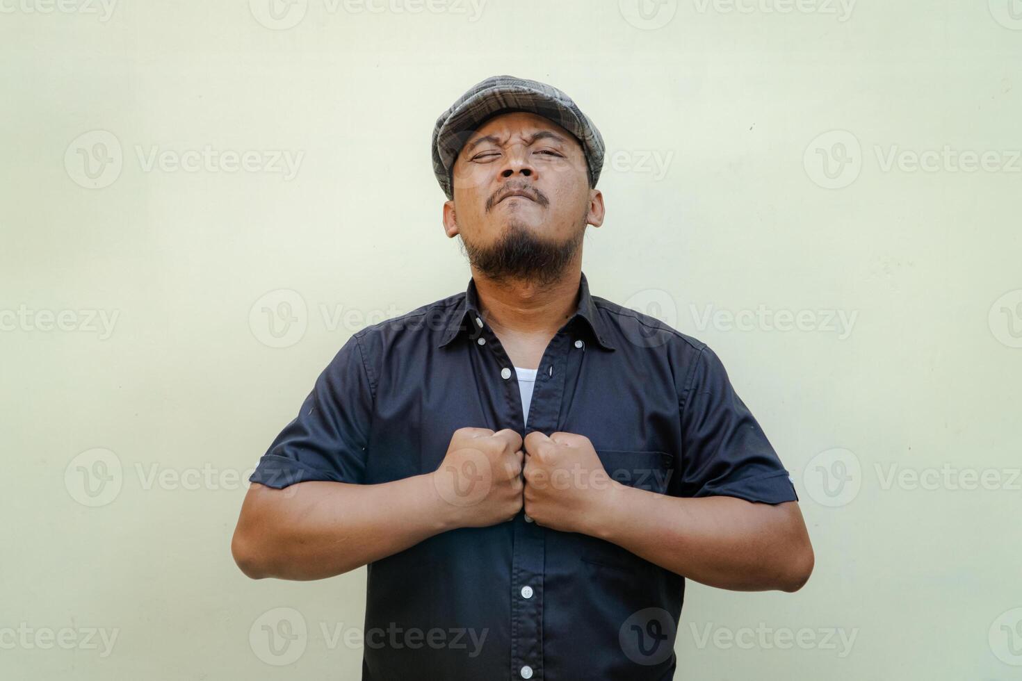 Half-length portrait of an adult Southeast Asian man posing in vintage style with black shirt and newspaper seller hat on beige background. photo