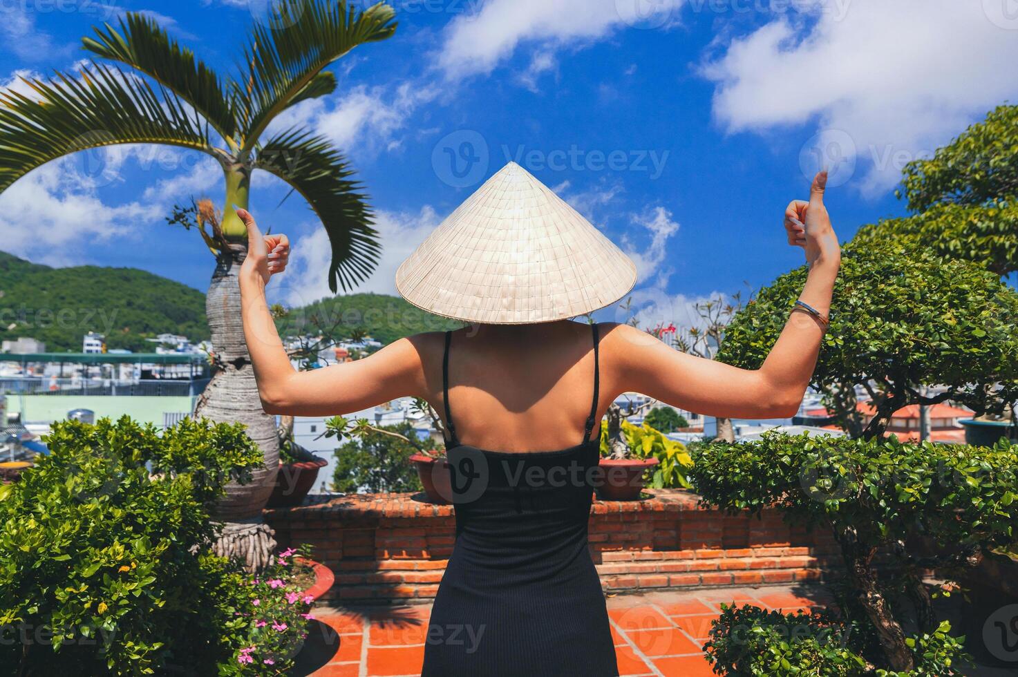 A young lady in a traditional Asian hat stands and looks at the Asian landscape. photo