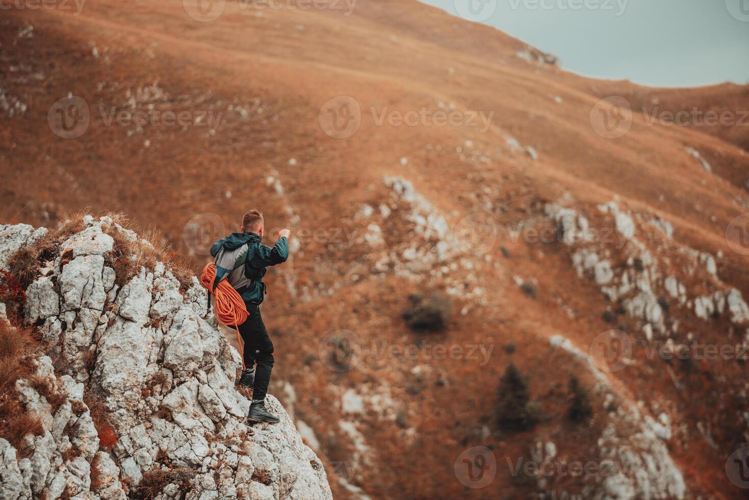 A happy male hiker or climber with arms up celebrating successfully completed a hiking or climbing route on the mountain peak adventure travel extreme sport outdoor. photo