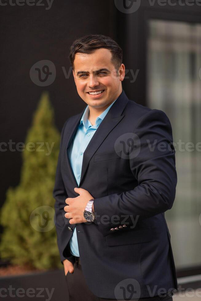 Portrait of a happy young business man standing near the office building looking at camera and smiling. photo