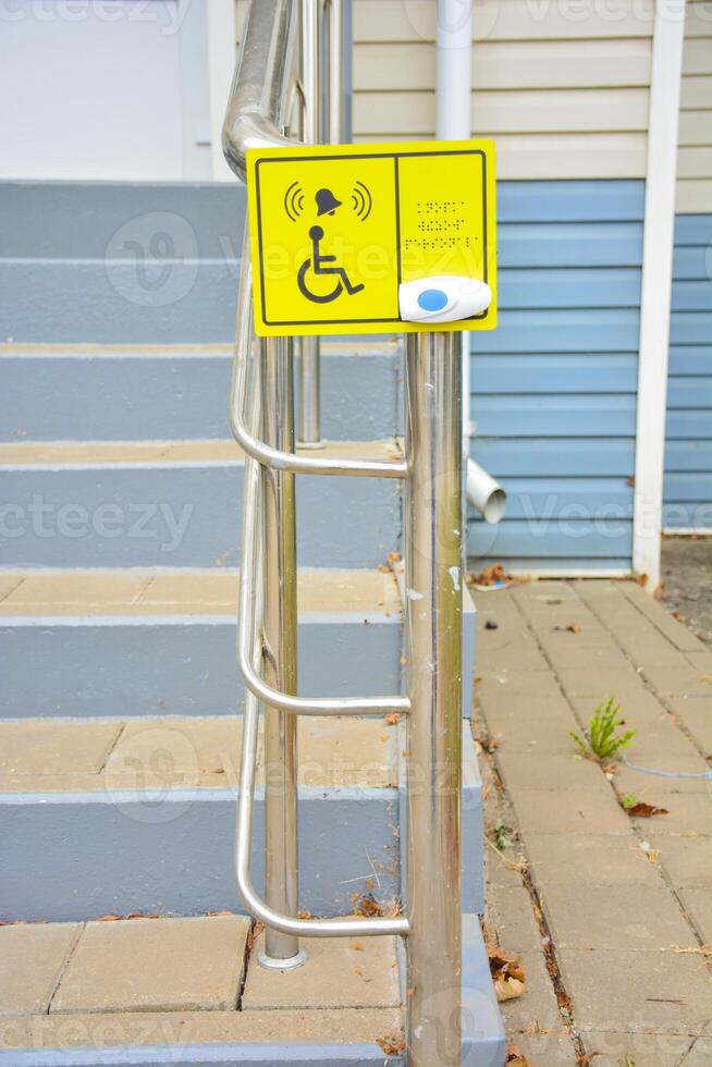 Yellow sign and call button outside of building with for people in wheelchair. Employee call button and braille text for blind people at the entrance to the drug store. Inclusive society photo