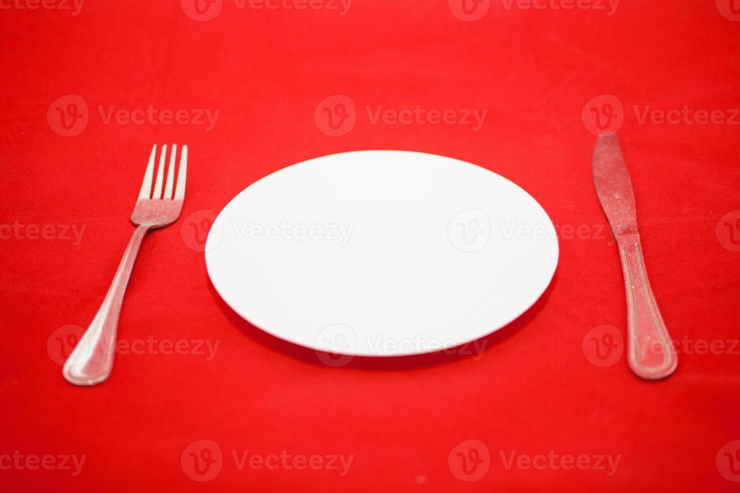 A white plate with a fork and knife on a red background photo