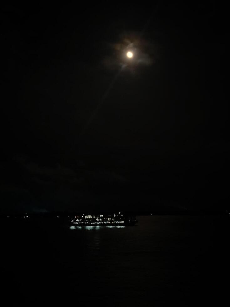 A boat is in the water at night with a full moon photo