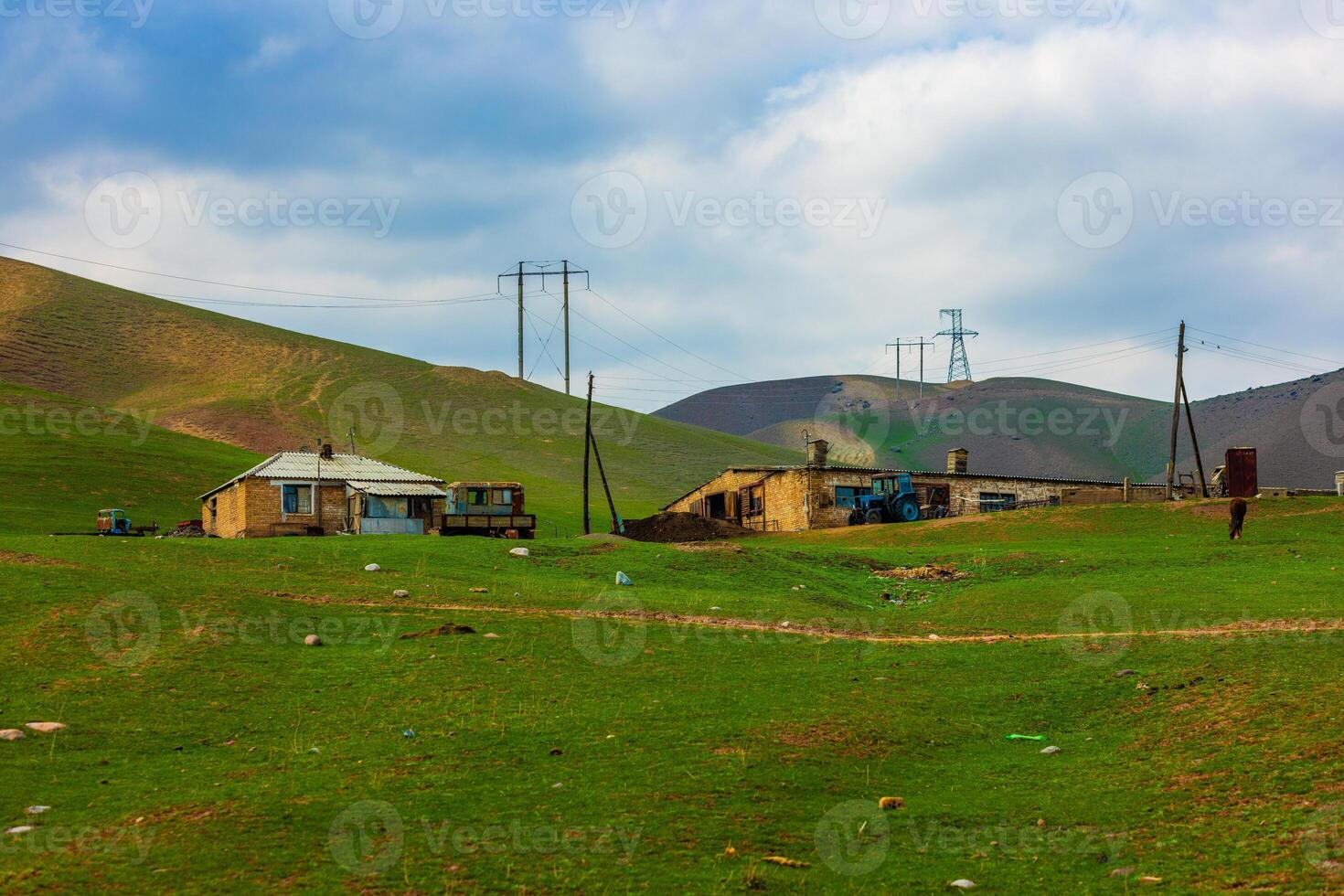 serene countryside landscape with rustic buildings, power transmission line supports and green foothills in the background photo