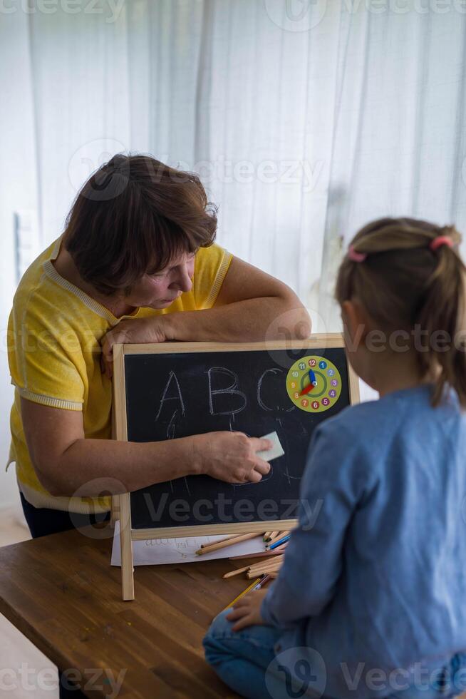 A determined 5-year-old girl focuses on writing letters with chalk on a board, engaging in her studies. photo