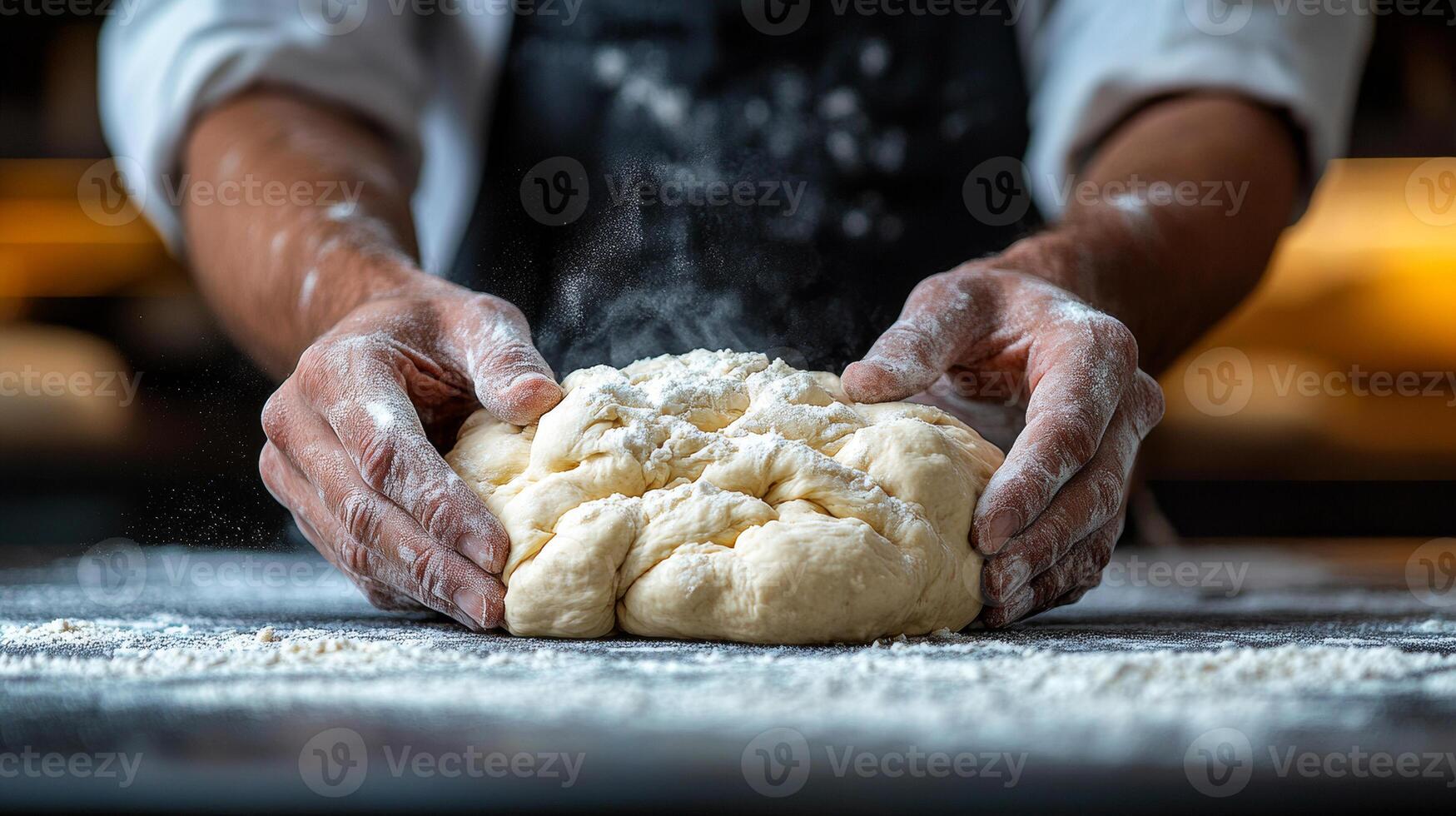 A man is making bread dough on a table. The dough is covered in flour and the man is holding it in his hands photo