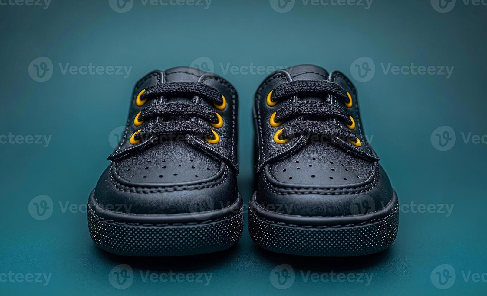 Two black shoes with yellow laces. The shoes are on a blue background. The shoes are shiny and have a metallic look photo