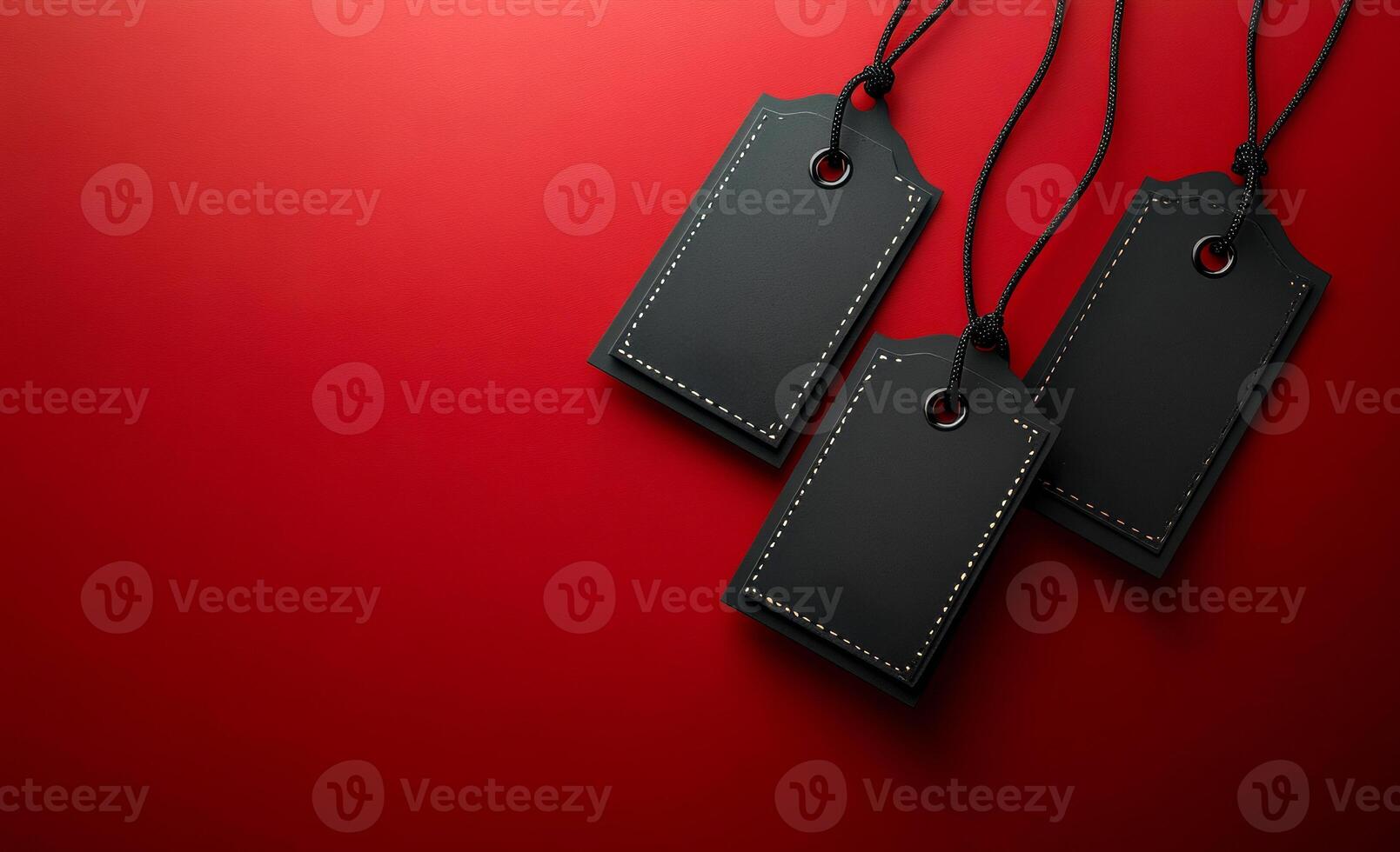 Three black tags are hanging from a red background. The tags are black and have a silver or gold design. The tags are hanging from a red background, which creates a sense of contrast photo