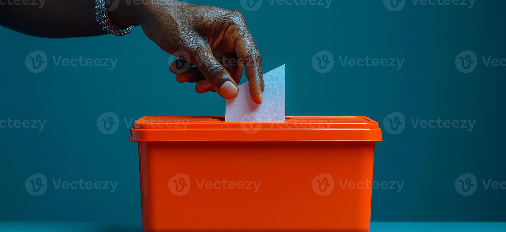 A hand casting a vote in an orange ballot box. A voter places their ballot into an orange box, symbolizing participation in the democratic process during the election. photo