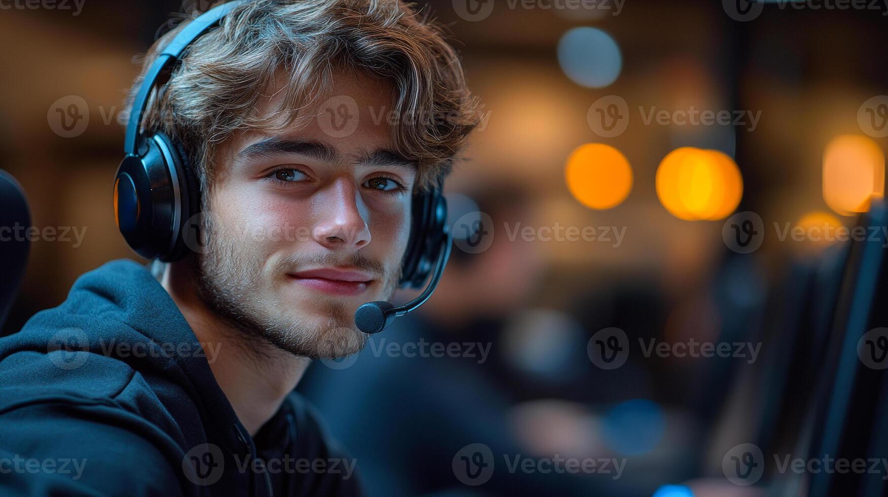 A man wearing headphones and a microphone is smiling. He is wearing a black hoodie and he is in a relaxed and comfortable mood photo