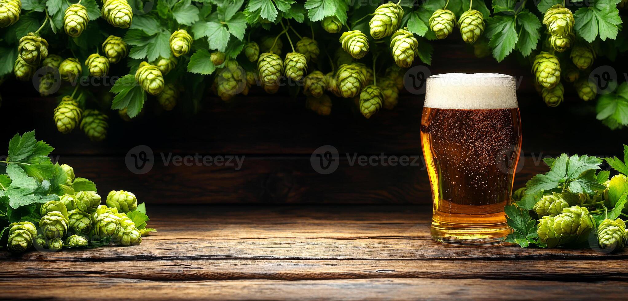 A glass of beer is on a wooden table with a bunch of green leaves. The leaves are in the foreground and the glass is in the background. Concept of relaxation and enjoyment photo