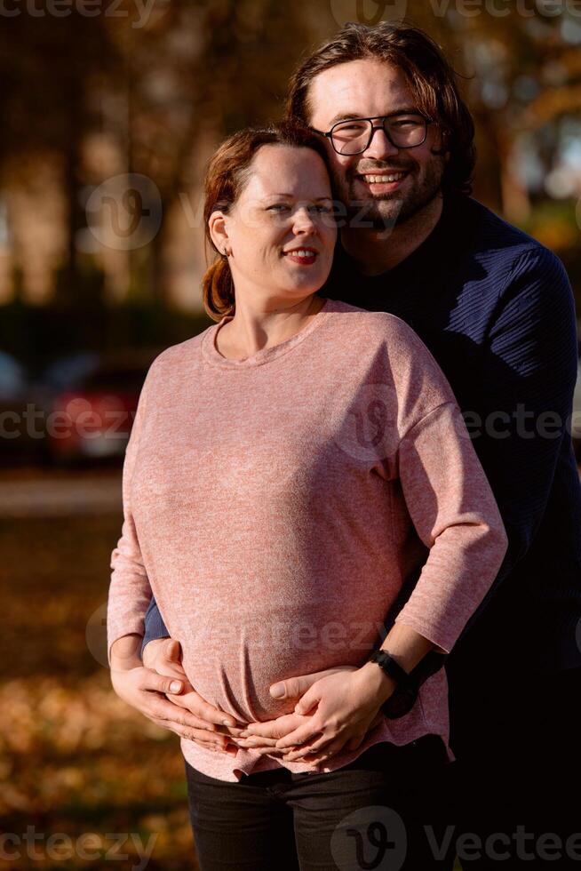 A man lovingly embraces his pregnant wife in the park, sharing a peaceful moment of warmth and affection photo