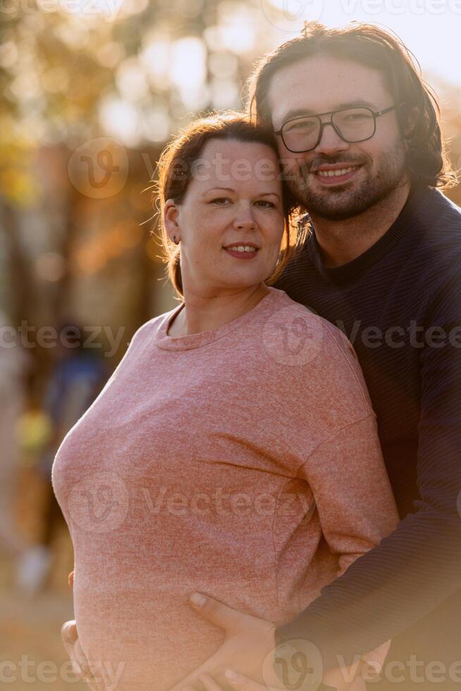 A man lovingly embraces his pregnant wife in the park, sharing a peaceful moment of warmth and affection photo