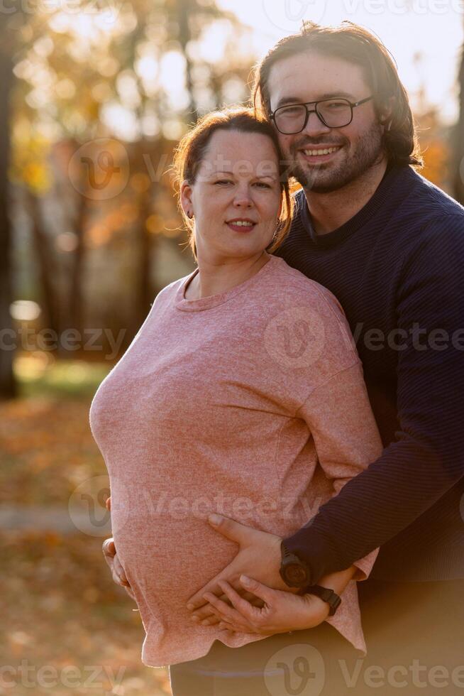 A man lovingly embraces his pregnant wife in the park, sharing a peaceful moment of warmth and affection photo