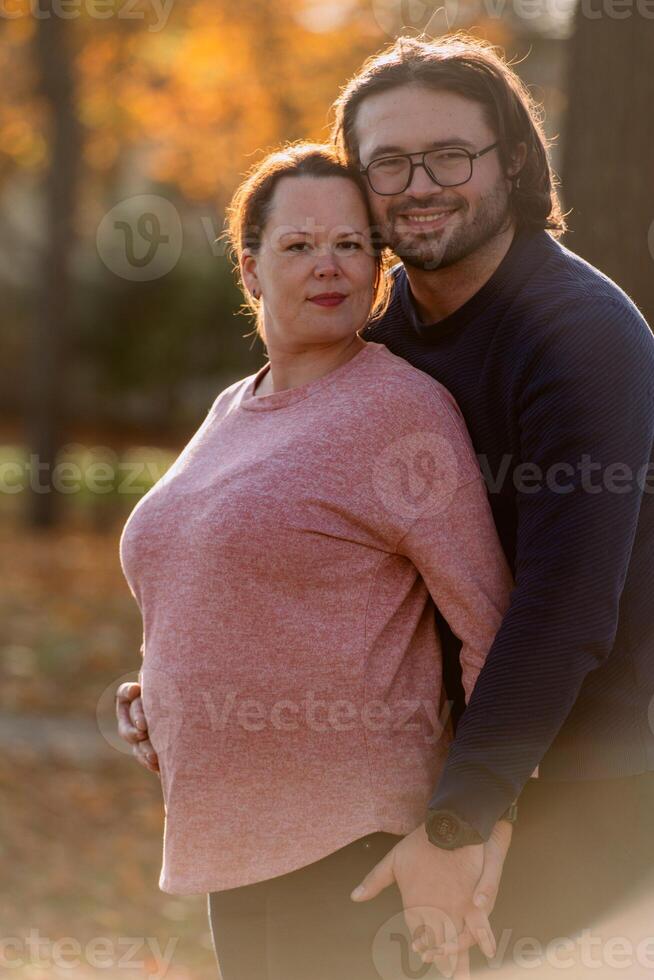 A man lovingly embraces his pregnant wife in the park, sharing a peaceful moment of warmth and affection photo