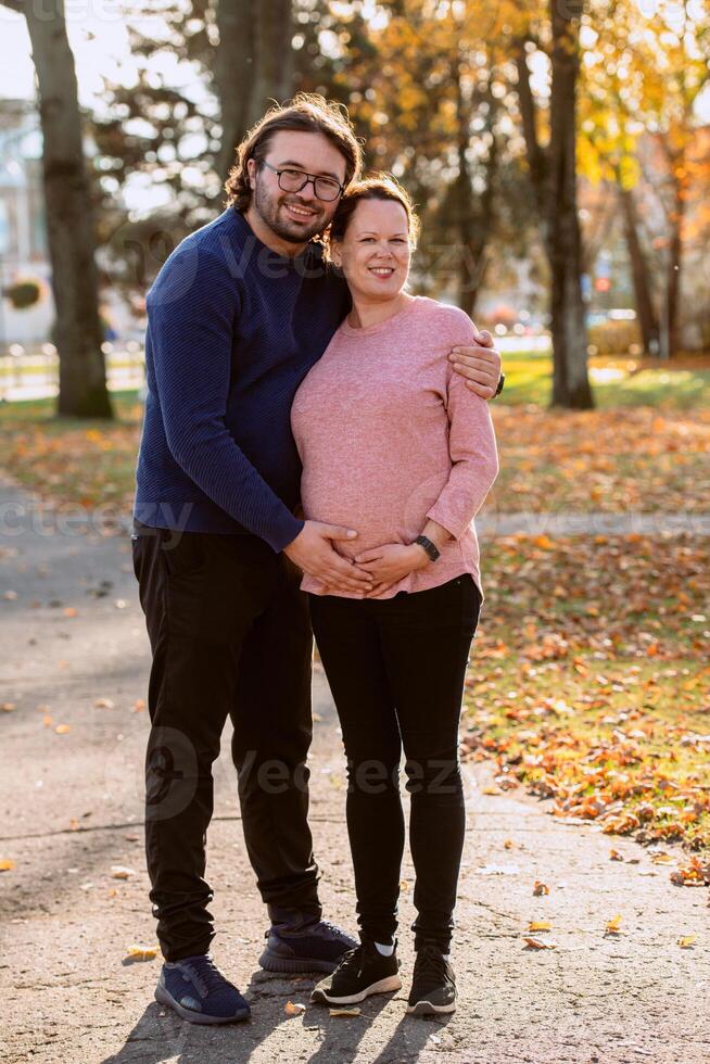 A man lovingly embraces his pregnant wife in the park, sharing a peaceful moment of warmth and affection photo