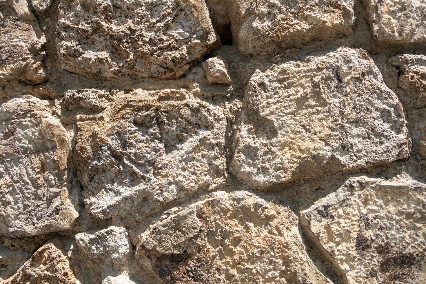 Close-up view of weathered stone wall featuring uneven textures and natural colors in sunlight photo