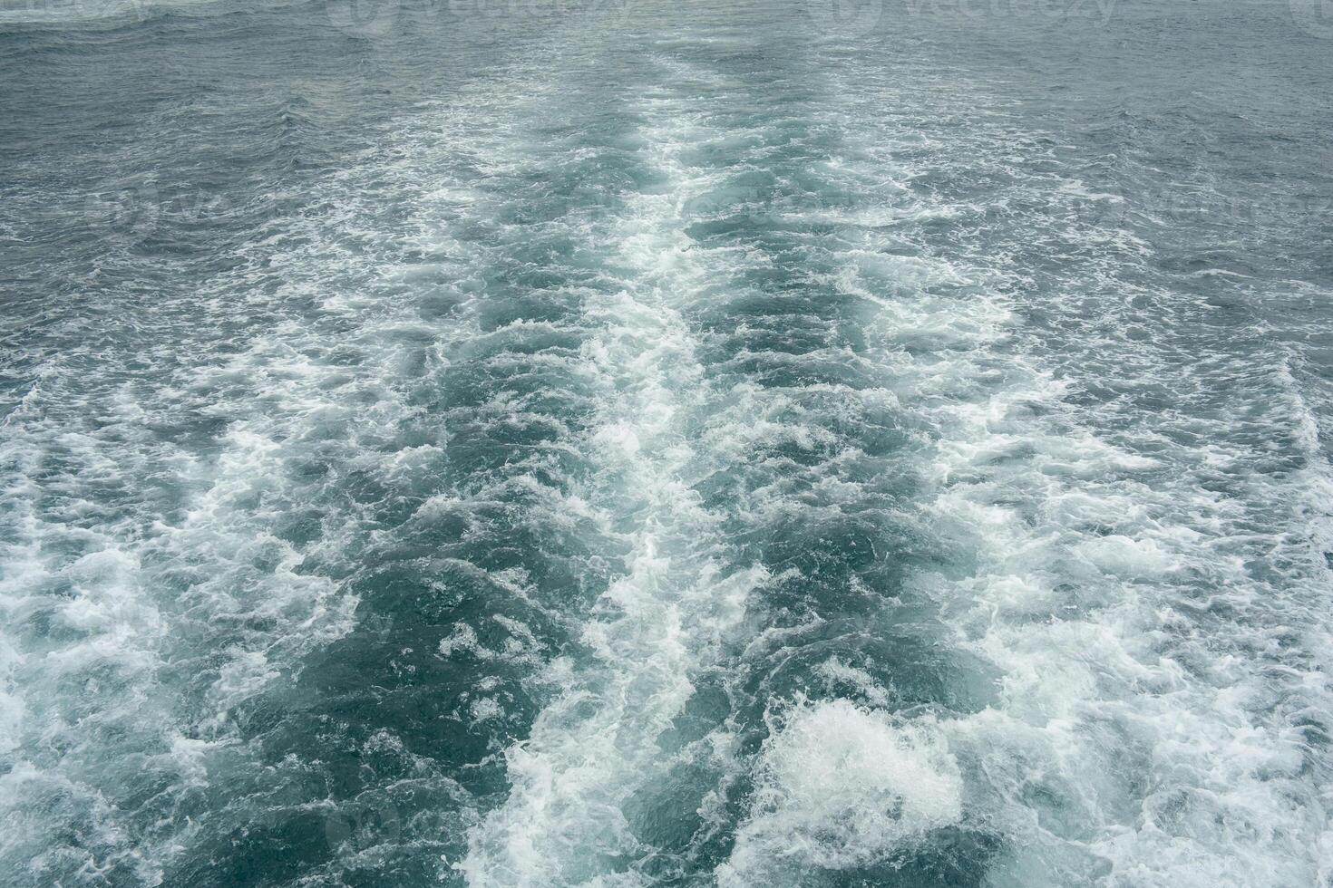 Rippling waves create dynamic patterns behind a boat as it moves through a serene sea under an overcast sky photo