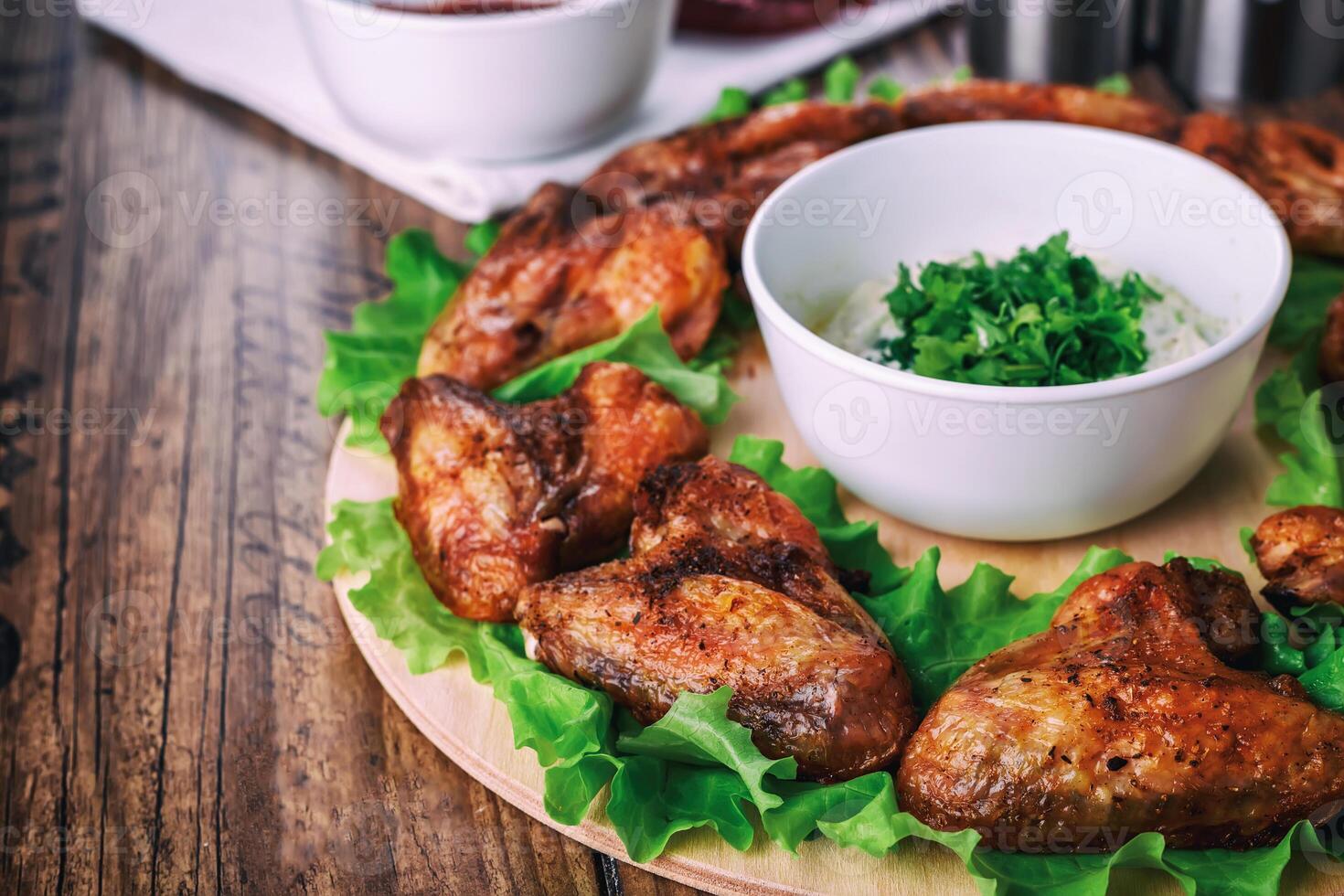 delicious grilled chicken wings with garlic and tomato sauce with lettuce on a round board on wooden rustic background photo
