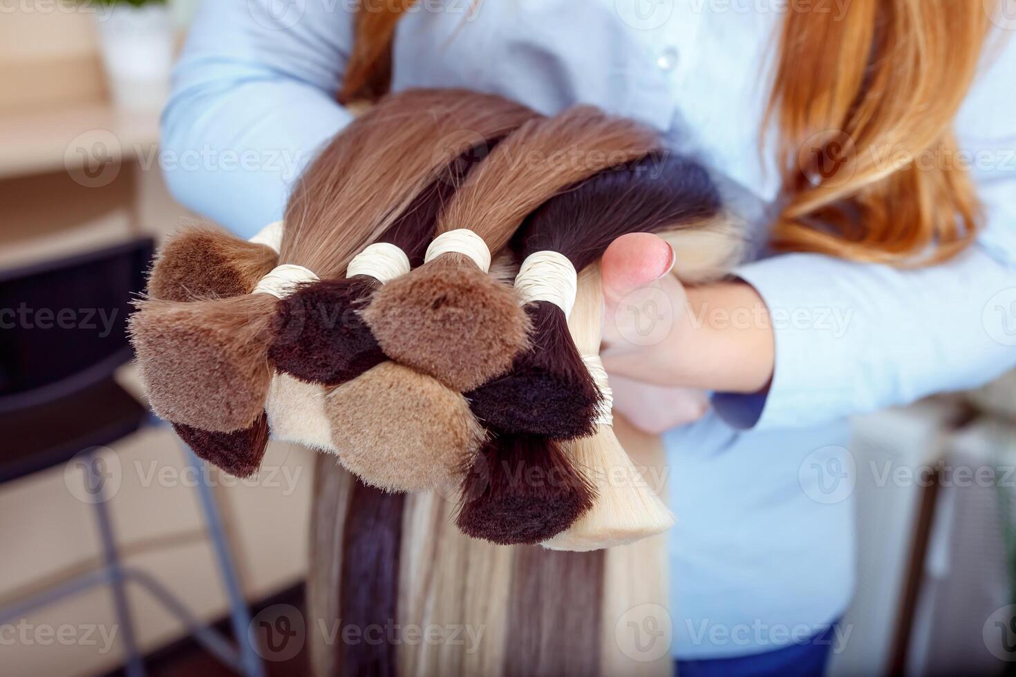Woman holds hair extension equipment of natural hair. hair samples of different colors photo