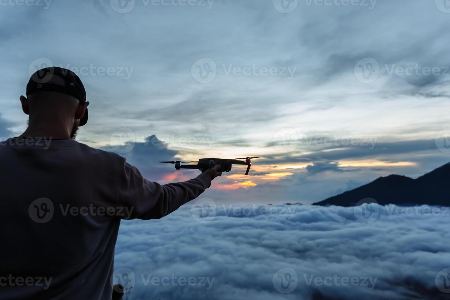Man tourist looks at the sunrise on the volcano Batur on the island of Blai in Indonesia. Hiker man launching a flying drone with a remote controller in his hand, travel concept photo
