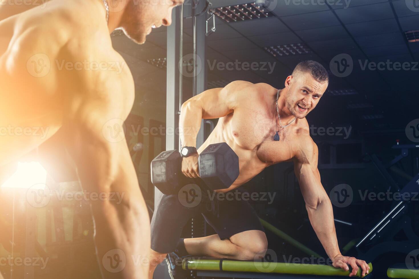 power athletic guy , execute exercise press with dumbbells, in sport hall photo