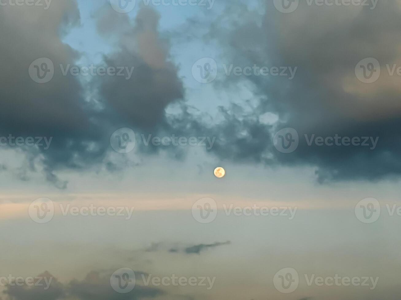 A serene twilight sky displays the moon amidst scattered clouds, creating a peaceful and contemplative atmosphere. The gentle hues of blue and gray enhance the tranquil evening scene. photo