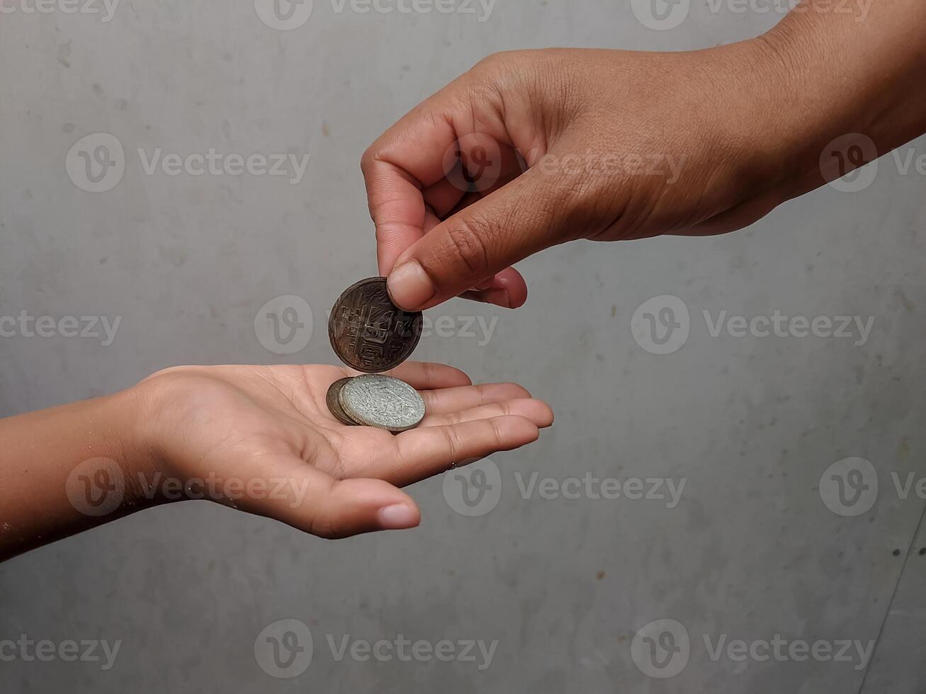 Two hands engaged in a coin exchange, highlighting themes of charity, giving, and economic interaction. The simple backdrop emphasizes the focus on human connection and finance. photo