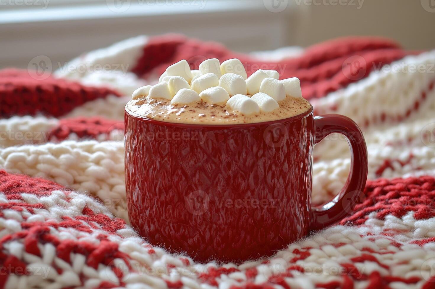 Red mug containing hot chocolate with marshmallows warming on a cozy christmas blanket photo